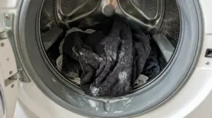 Asciugamani scuri nel cestello della lavatrice con residui di detersivo visibili sul bucato e sulla guarnizione