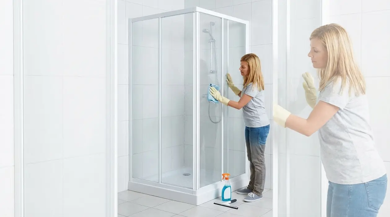 Donna pulisce una cabina doccia in plastica con panno e detergente in un bagno luminoso