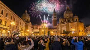 Folla in piazza festeggia Capodanno con fuochi d'artificio sopra edifici storici in Italia.