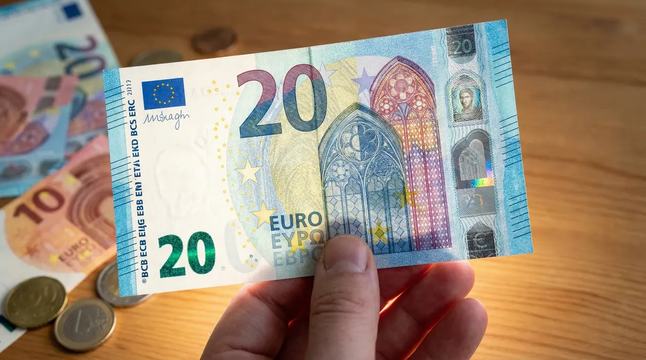Una mano tiene una banconota da 20 euro alla luce su un tavolo in legno
