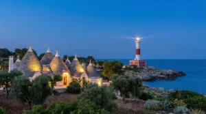 Trulli illuminati al tramonto con un faro sulla costa sullo sfondo
