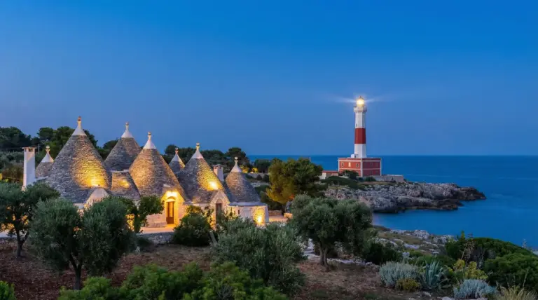 Trulli illuminati al tramonto con un faro sulla costa sullo sfondo