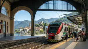 Un treno regionale in partenza da una stazione con passeggeri e vista su lago e montagne
