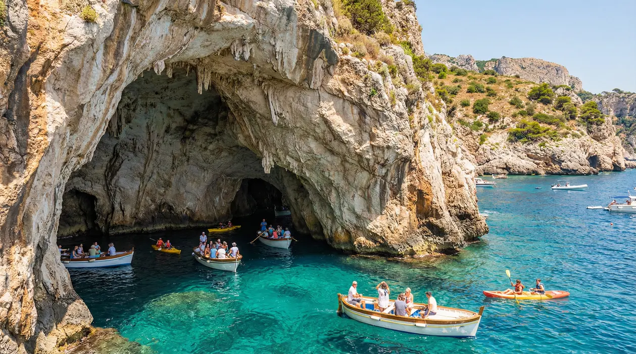 Barche con turisti davanti all'ingresso di una grotta marina in Italia, in acque cristalline