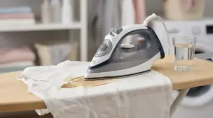 Ferro da stiro su una maglietta bianca bruciata sull’asse da stiro, con bicchiere d’acqua accanto