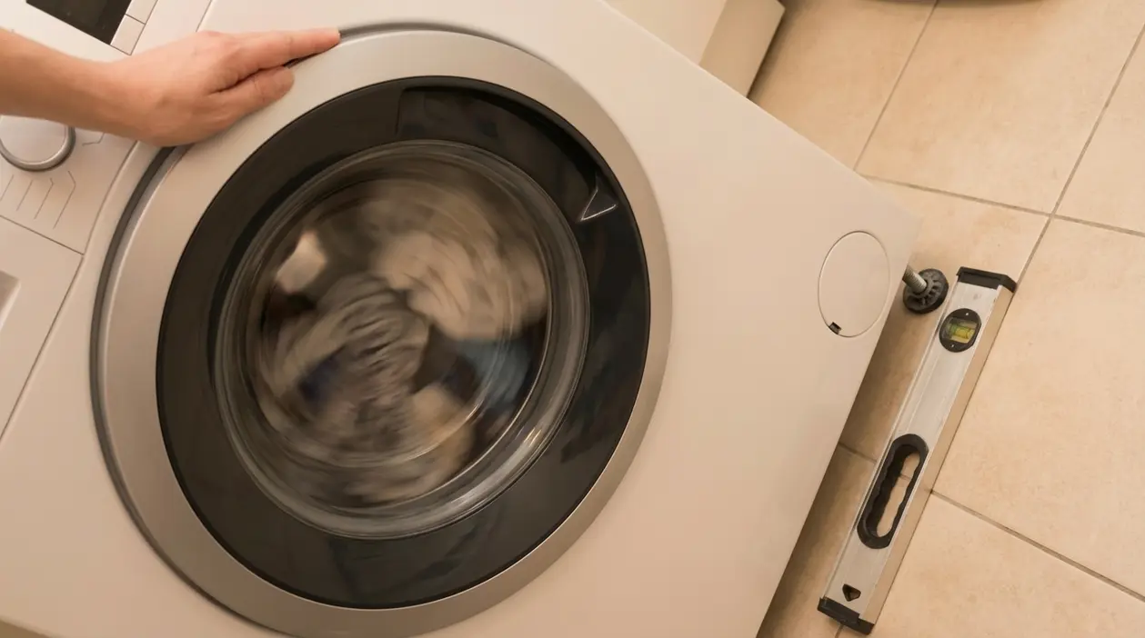 Mano su lavatrice in centrifuga con bolla di livello sul pavimento, per controllare la stabilità e ridurre le vibrazioni