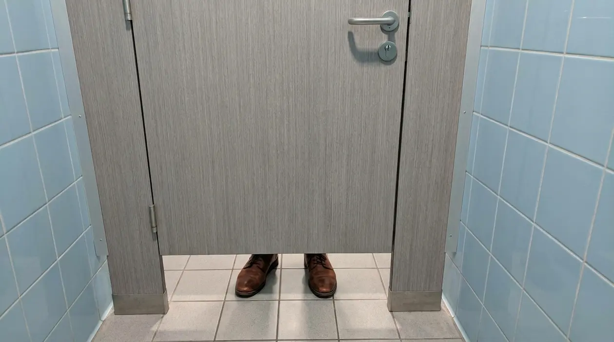 Porta di un bagno pubblico con spazio inferiore visibile e una persona all'interno