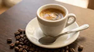 Tazzina di caffè espresso su piattino bianco con cucchiaino e chicchi di caffè sul tavolo