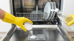 Mani con guanti versano bicarbonato e aceto nella lavastoviglie aperta per una pulizia naturale