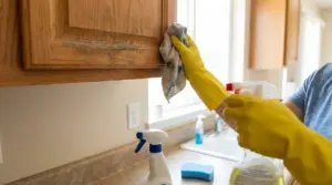 Persona con guanti gialli pulisce un pensile della cucina con panno e spray detergente