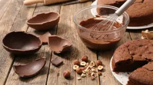 Uova di Pasqua spezzate, ciotola di cioccolato fuso, torta al cioccolato e nocciole su tavolo di legno