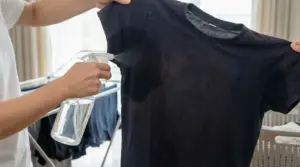 Una persona spruzza liquido sotto le ascelle di una maglietta scura