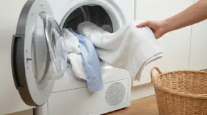 Una persona carica asciugamani e camicie nell’asciugatrice per asciugare i panni evitando pieghe e stropicciature.