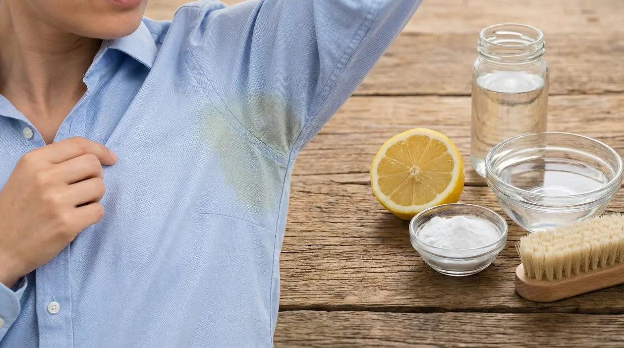 Macchie gialle di sudore sotto l’ascella su camicia azzurra, con limone, bicarbonato, acqua e spazzola su tavolo